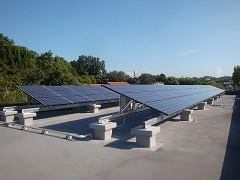 青空の下、林に囲まれた場所に建てられている2つの太陽光発電システムの写真