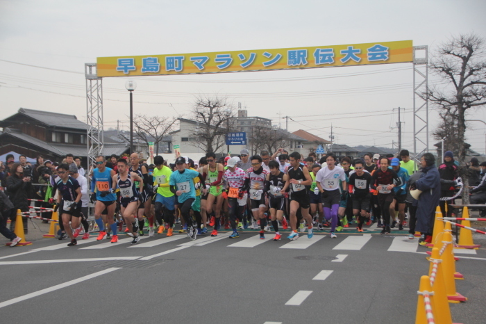 早島町マラソン駅伝大会の横断幕からスタートするゼッケンを付けた大勢のランナーたちの写真