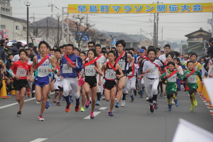 早島町マラソン駅伝大会の横断幕からスタートする大勢のゼッケンとたすきを掛けたランナーたちの写真