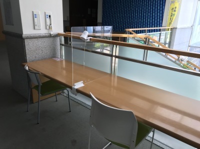横長の机に透明のアクリル板のパーテーションが設置されていて奥に大きなガラスがあるカウンターの写真