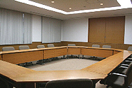 机が六角形に並べられた椅子のたくさんあるやや大きめの集会室の写真