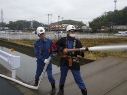 2人のヘルメットを被った消防団員が2人でホースを持って放水をしている写真