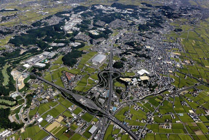 高速道路や大小さまざまな建物、林や水田などの沢山の緑に囲まれた早島町の航空写真