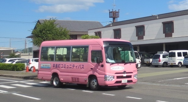 ピンク色した小さなコミュニティバスが道路を走行している写真