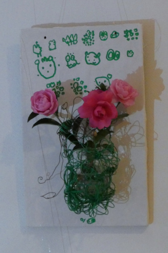 壁に動物の顔が描かれている布に3つのバラの花が糸でぐるぐる巻きにされている写真