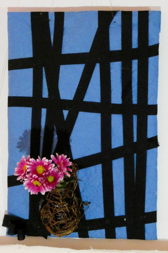 青い布に黒の格子状の線が描かれていて左下にピンクの花が飾られている写真