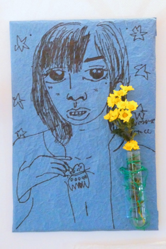青色の布に人物が描かれていて右下に黄色い花が緑色の糸でぐるぐる巻きにされている写真