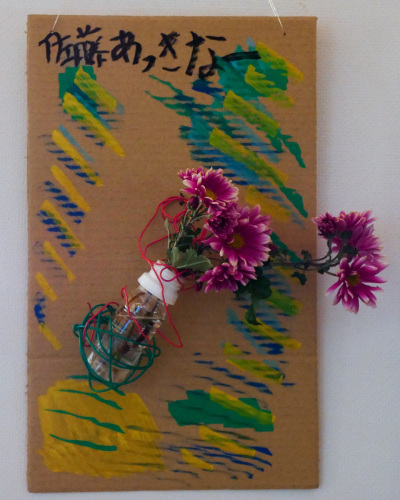 佐藤あっきなーと書かれたダンボールの板に紫色の花が緑色の糸でぐるぐる巻きにされている写真