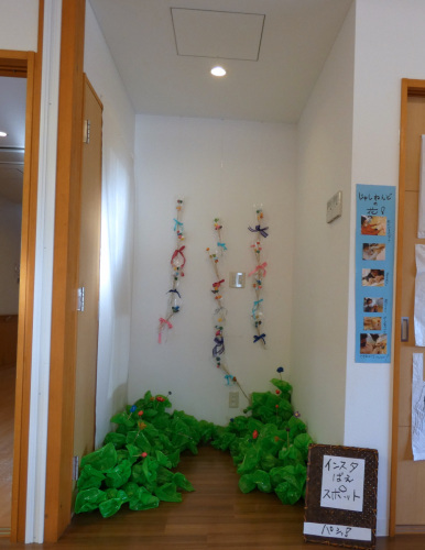 部屋の奥の壁にリボンの付いた樹脂粘土の花が三列飾られている写真